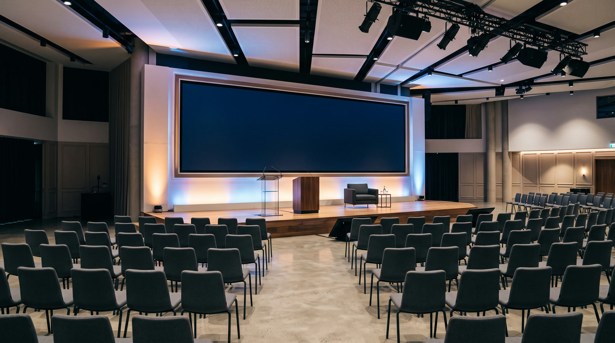 A beautifully lit corporate conference stage with elegant uplighting and neat rows of seating